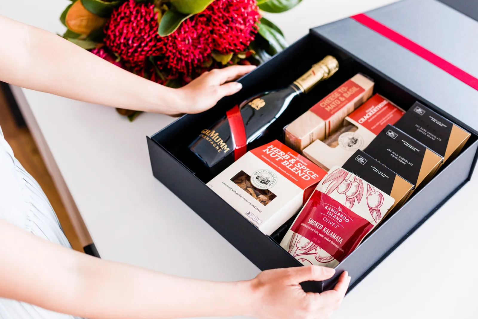 Open black gift hamper box filled with Valley Produce Co nuts and crackers, Kangaroo Island smoked olives, chocolates and sparkling wine