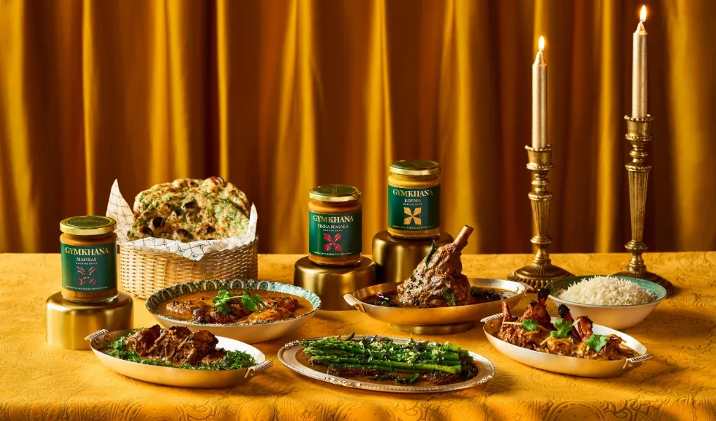 Gymkhana Fine Foods cooking sauces on a gold table set with Indian dishes, naan and candles